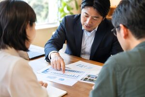 机上の提案書のグラフを指して説明する40代男性の手元