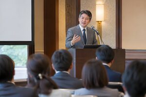 ホテルの会場で演台に立ち講演する50代男性