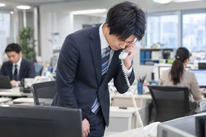 受話器を持ったまま軽く頭を下げて応対する20代男性