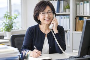 笑顔で電話応対をする眼鏡の50代女性