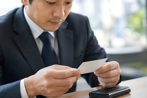 受け取った名刺を両手で持って確認する男性の手元