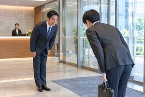 オフィスの入口で来客と互いにお辞儀をして迎える40代男性