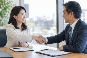 合意に達しテーブル越しに握手する30代女性と50代男性