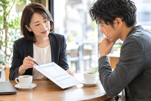 カフェのテーブルで見積書を示す40代女性と検討する取引先