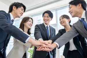 オフィスで円になって手を重ねる5人の若手社員