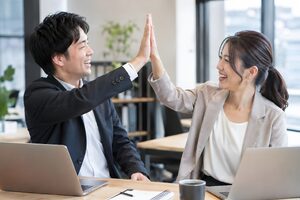 プロジェクト完了を祝ってデスク越しにハイタッチする同僚