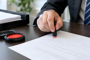 決裁書類に赤い印鑑を押す男性の手元