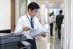 コピー機の前で印刷した書類をそろえる40代男性