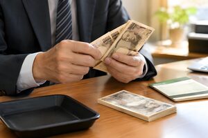 デスクで一万円札を数える男性の手元と通帳