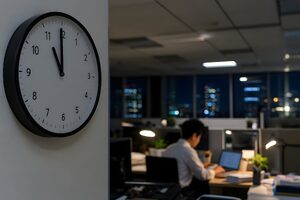 夜11時を指す壁時計とデスクで作業を続ける社員