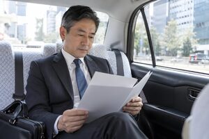 タクシーの後部座席で資料に目を通す50代男性