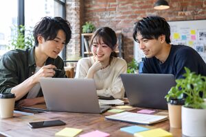 ロフト風の小さなオフィスで並んで働く20代の創業メンバー3人