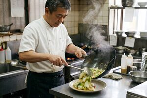 八宝菜を皿に盛る料理人