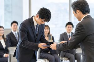 社内表彰式で上司から賞状とトロフィーを受け取る20代男性