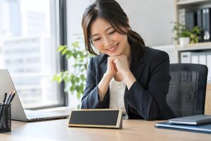 新しい役職の名札をデスクに置いて誇らしげに微笑む30代女性