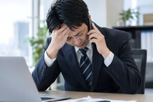 電話で頭を下げながら謝罪する30代男性