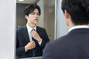 会議の前に鏡でネクタイを直す20代男性