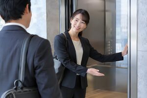 エレベーターの扉を押さえて来客を先に通す30代女性