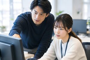 同じモニターを見ながら画面を指して相談する2人の社員
