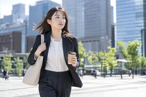 朝の駅前広場をコーヒーを手に足早に歩く20代女性