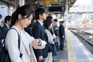朝のホームで腕時計を確認しながら電車を待つ30代女性