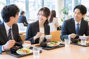 社員食堂で定食を囲んで談笑する3人の社員