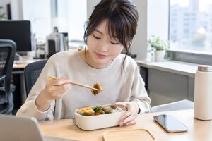 昼休みにデスクで手作り弁当を食べる20代女性