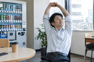 休憩室で腕を上げて伸びをする40代男性