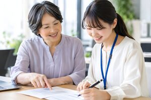若手社員に書類を指して教える60代の女性ベテラン