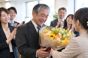 定年退職の日に同僚から花束を受け取る60代男性