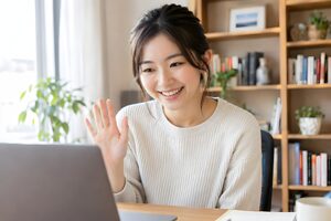 オンライン会議の冒頭でカメラに手を振って挨拶する20代女性