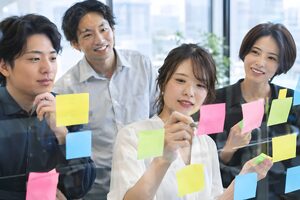 ガラスの壁にカラフルな付箋を貼ってブレストをする4人のチーム