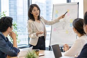 フリップチャートの案を指しながら議論を進行する40代女性