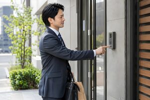 取引先の入口でインターホンを押す30代の営業マン