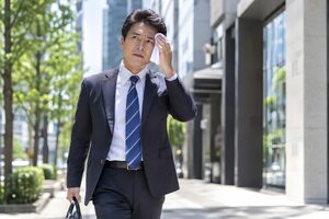 暑い日にハンカチで汗を拭きながら外回りをする40代の営業マン