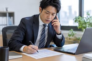 トークスクリプトを横に置いて電話営業をする30代男性