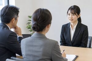 面接官2人の前で姿勢よく答える黒いスーツの20代女性