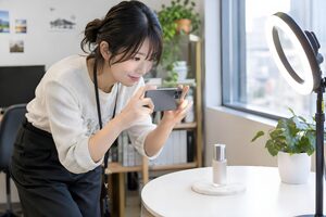 リングライトの下でスマートフォンで商品を撮影する20代のSNS担当者