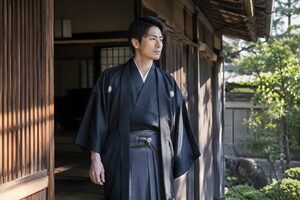 羽織袴を着て町家の玄関に立つ30代男性
