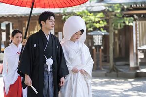 神社で白無垢と紋付袴の新郎新婦が番傘の下を歩く和婚
