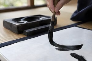 半紙に太い筆で線を書く手元のクローズアップ