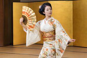 金屏風の前で扇を開いて舞う30代の日本舞踊の踊り手