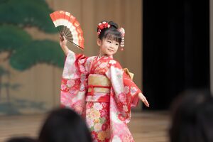 発表会で小さな扇を持って踊る7歳くらいの女の子