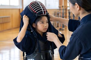 道場で先生に手伝ってもらい面をつける小学生