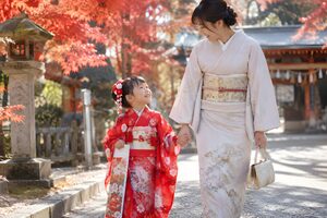 秋の参道で母と手をつないで歩く7歳の女の子