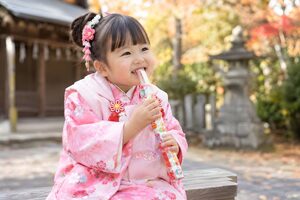 境内のベンチで千歳飴を食べる3歳の女の子