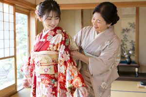 成人式の朝に娘の振袖の帯を結ぶ母親