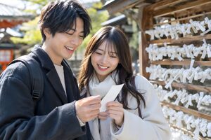 神社でおみくじを読んで笑い合う若いカップル