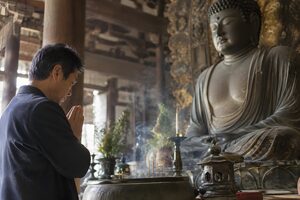 寺の本堂で仏像の前で合掌する50代男性