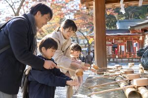 手水舎で柄杓を使って手を清める家族